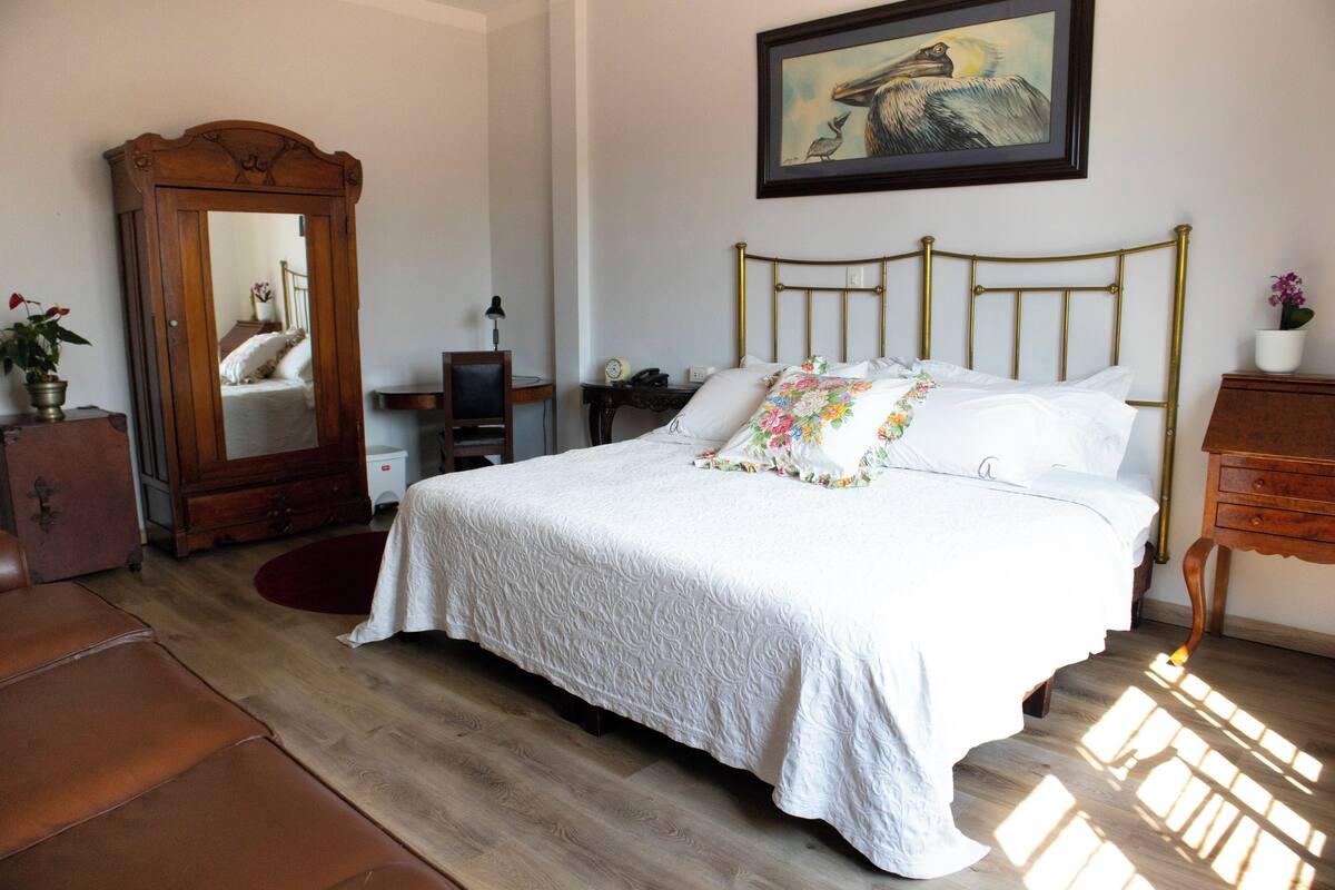 A bedroom with a bed, a dresser, a mirror, a desk, and a painting on the wall.