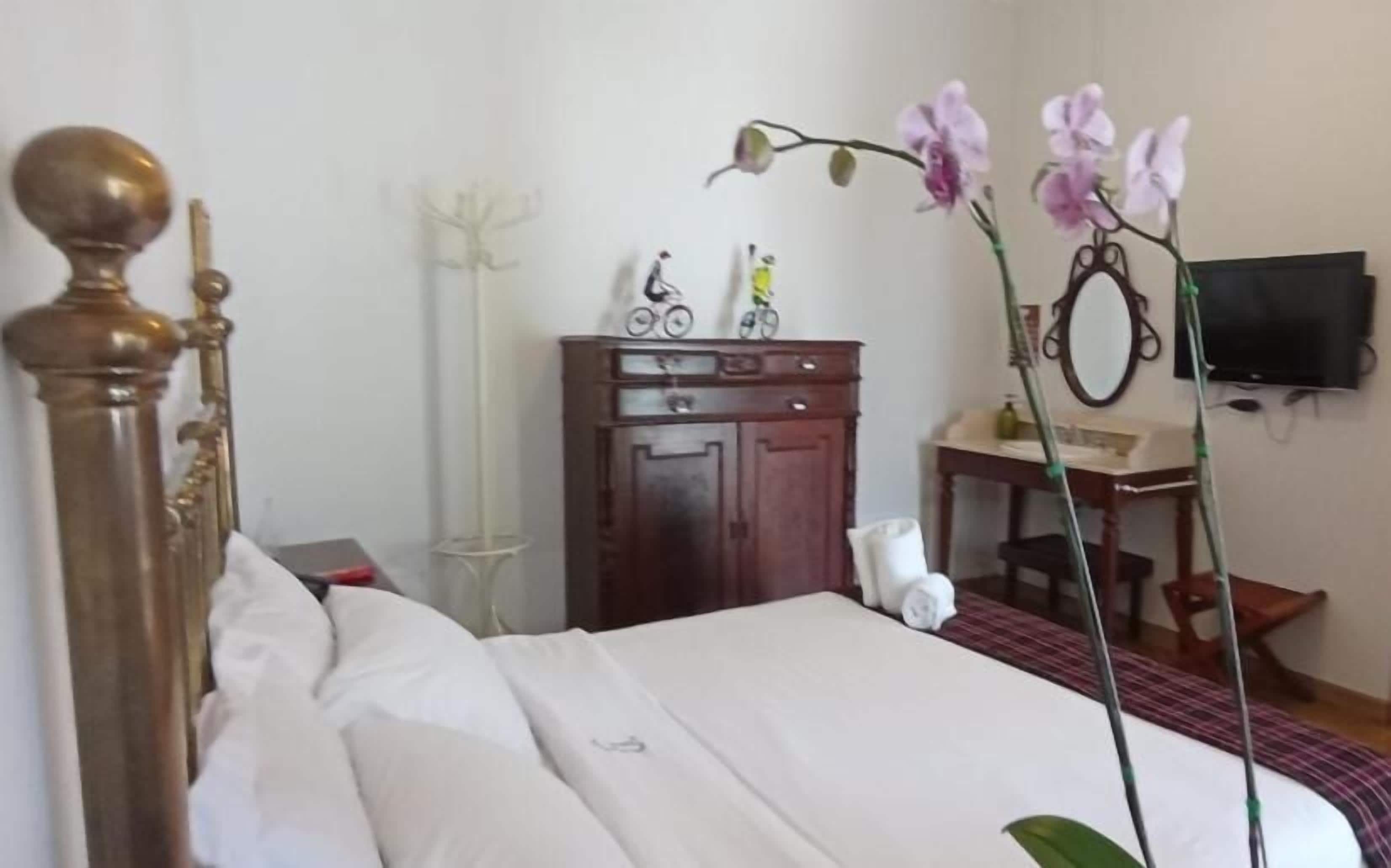 A hotel room with a bed, a wooden dresser, a desk with a mirror, and a television on the wall.