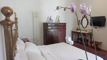 A hotel room with a bed, a wooden dresser, a desk with a mirror, and a television on the wall.