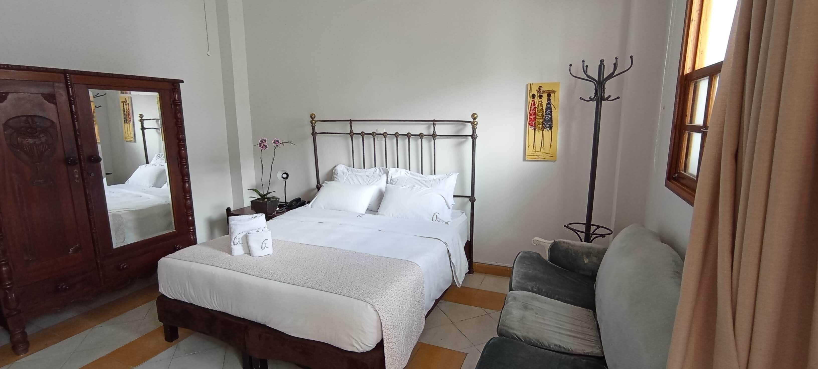 Un dormitorio ordenado con cama, armario, mesita de noche con lámpara y ventana con cortinas.