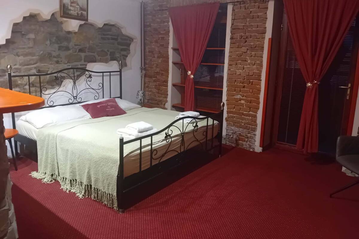 Een slaapkamer met een bed, een tafel, een stoel en een rood tapijt.