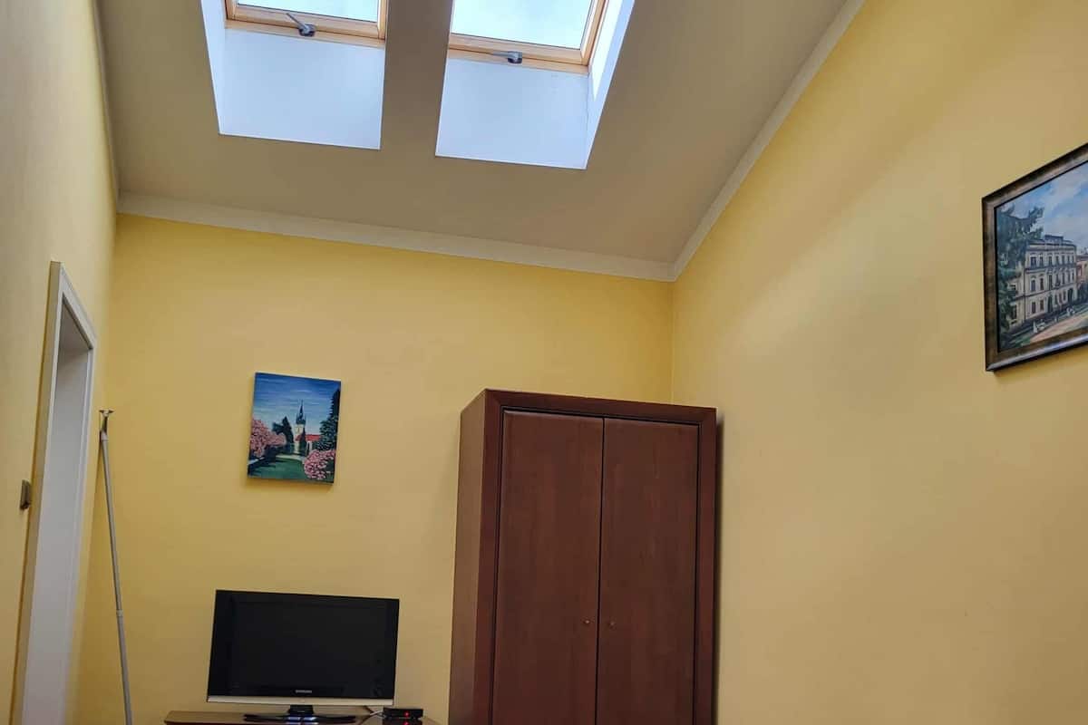 Een kamer met een bed, een bureau met een computer, een kledingkast en een schilderij aan de muur.