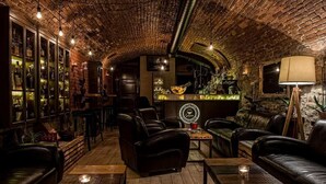 A cozy bar area with leather seating, a brick ceiling, and a bar counter with various bottles.
