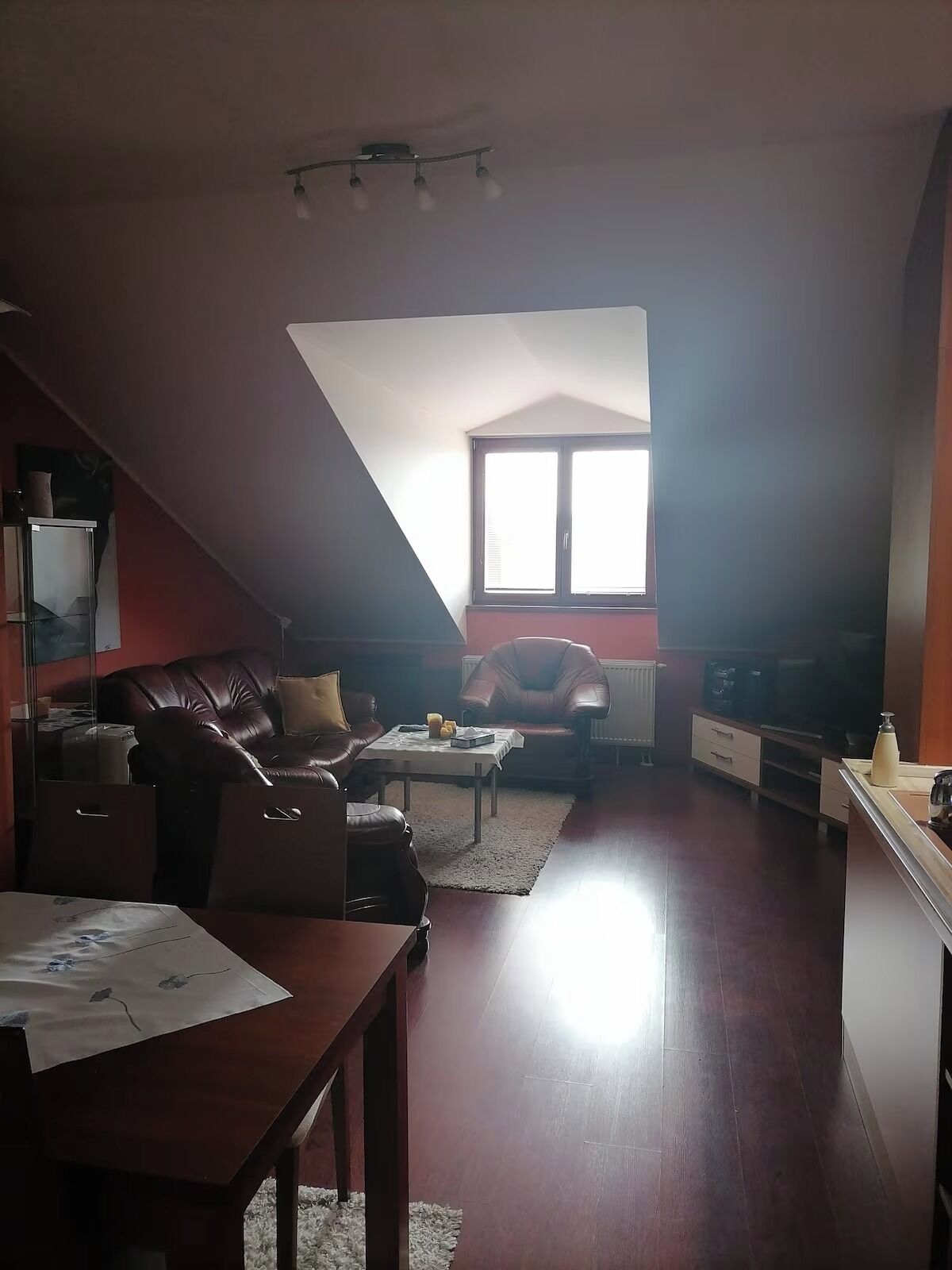Ein gemütliches Wohnzimmer mit schrägen Wänden, einem großen Fenster, einem Fernseher und einem Kamin.