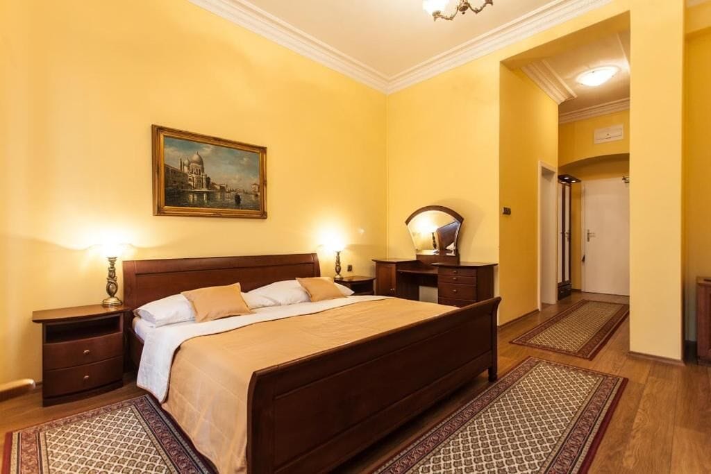 Habitación de hotel con una cama grande, una mesita de noche, una lámpara, un espejo y un cuadro en la pared.