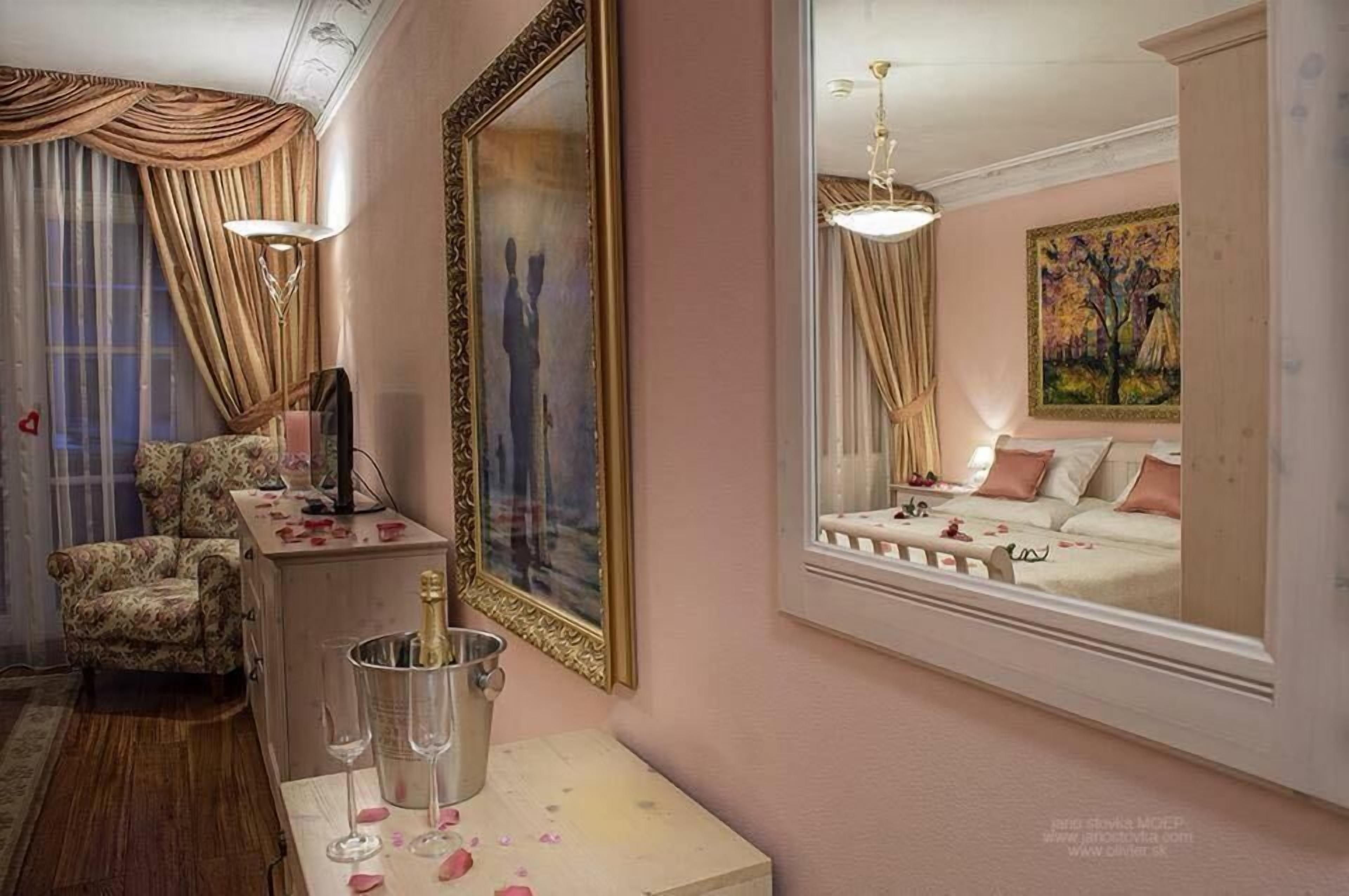 Une pièce comprenant un lit, une chaise, un bureau avec une lampe, un miroir et un tableau accroché au mur.
