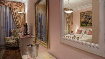 Une pièce comprenant un lit, une chaise, un bureau avec une lampe, un miroir et un tableau accroché au mur.