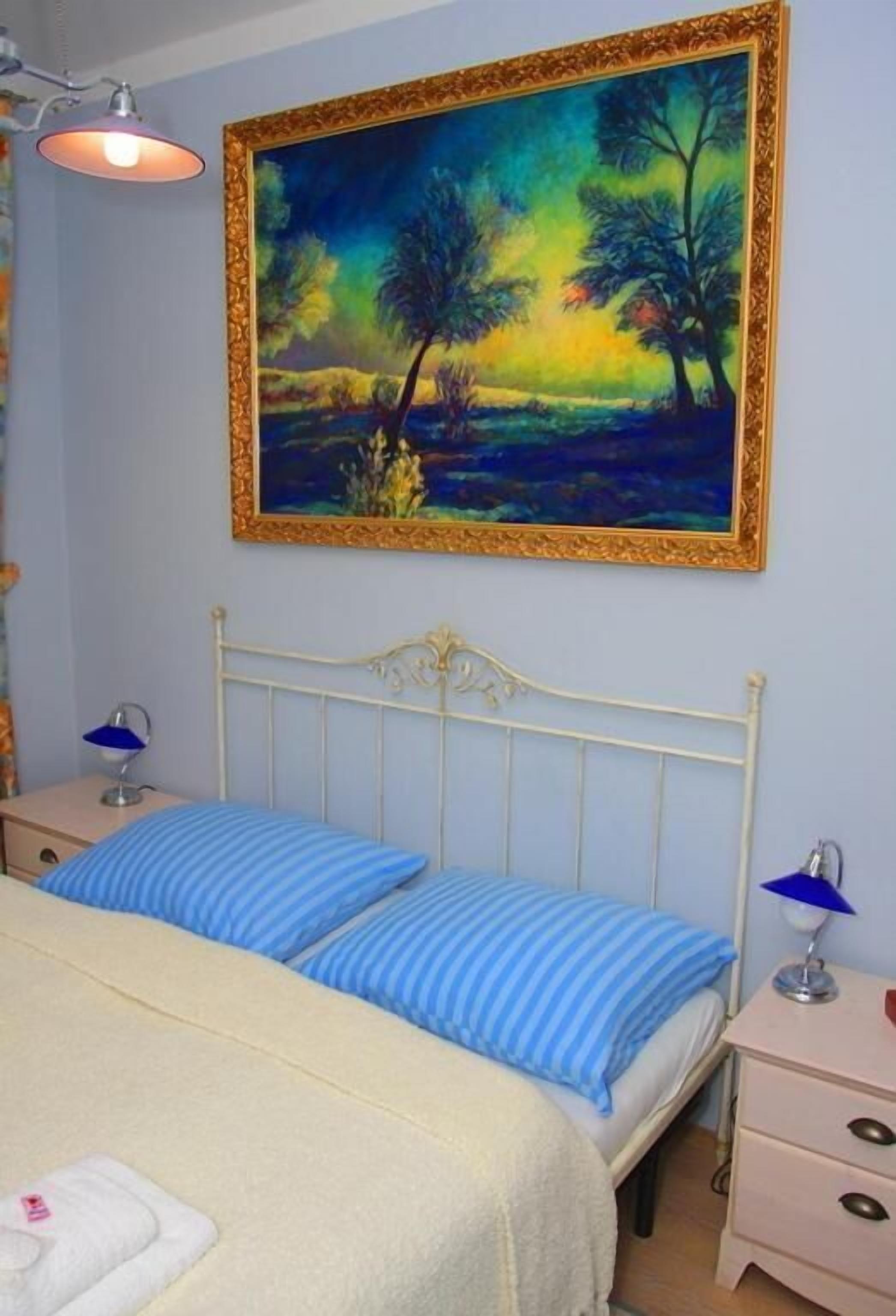 Un dormitorio con una cama, dos mesitas de noche, una lámpara y un cuadro en la pared.