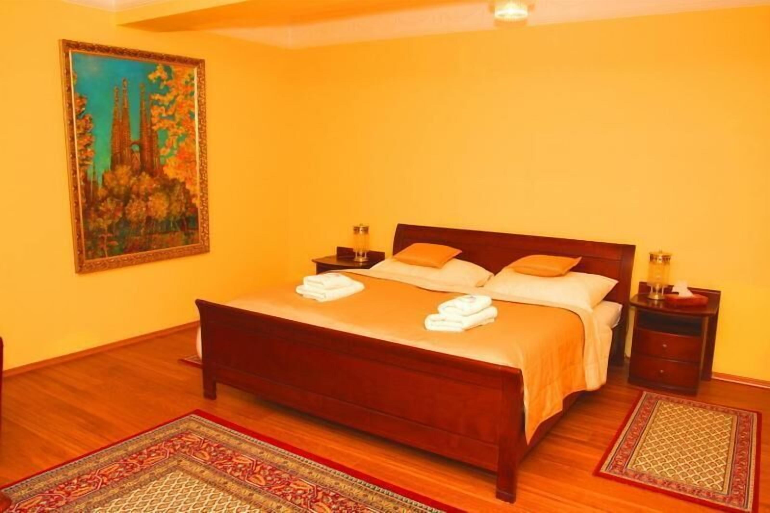 Een slaapkamer met een houten bed, twee nachtkastjes, een wandlamp en twee vloerkleden.