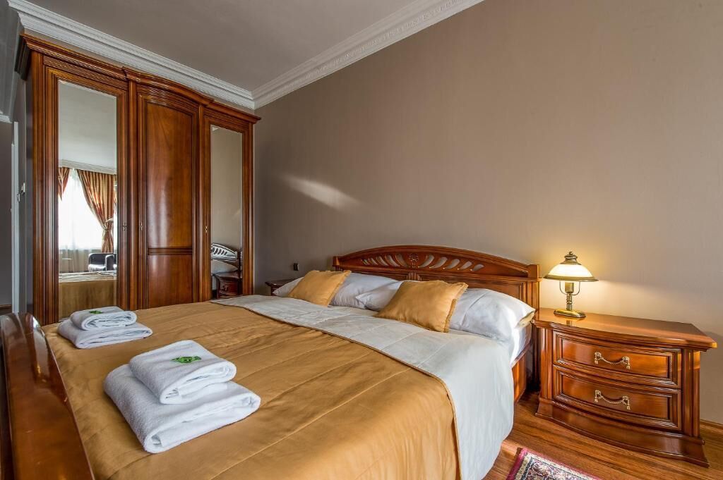 Una habitación de hotel con una cama grande, cabecera de madera, una mesita de noche con lámpara y un espejo.