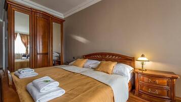 Una habitación de hotel con una cama grande, cabecera de madera, una mesita de noche con lámpara y un espejo.