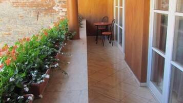 Un patio cubierto con piso de baldosas, pared de ladrillo y una hilera de macetas con flores.