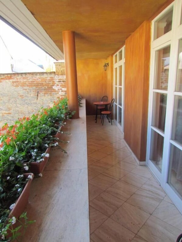 A covered patio with a tiled floor, a brick wall, and a row of potted plants with flowers. - Boutique Hotel Carpe Diem (Prešov)