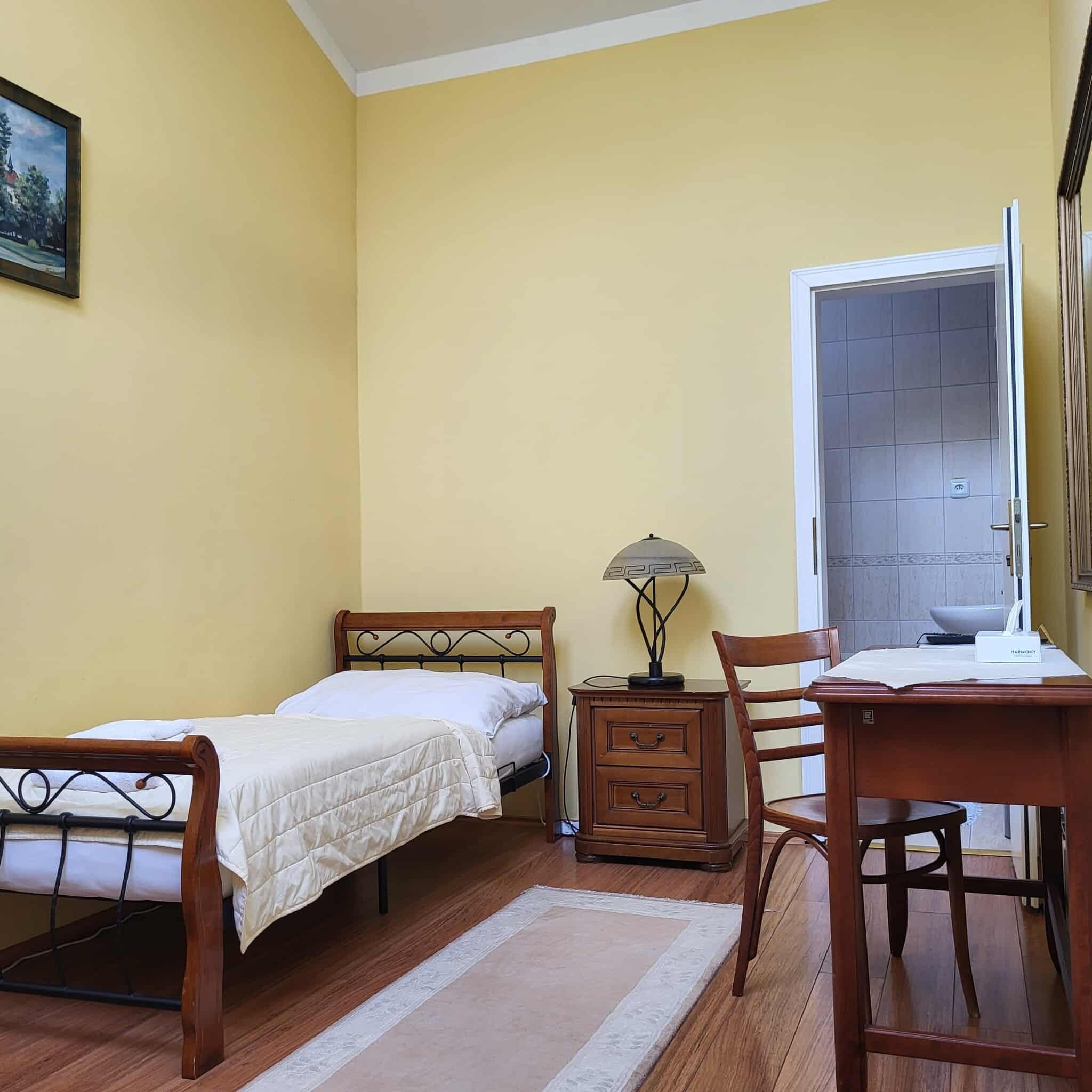 A bedroom with a bed, bedside table, lamp, chair, and a desk with a chair.