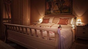A bedroom with a wooden bed, two bedside tables with lamps, a large painting on the wall, and a wardrobe.