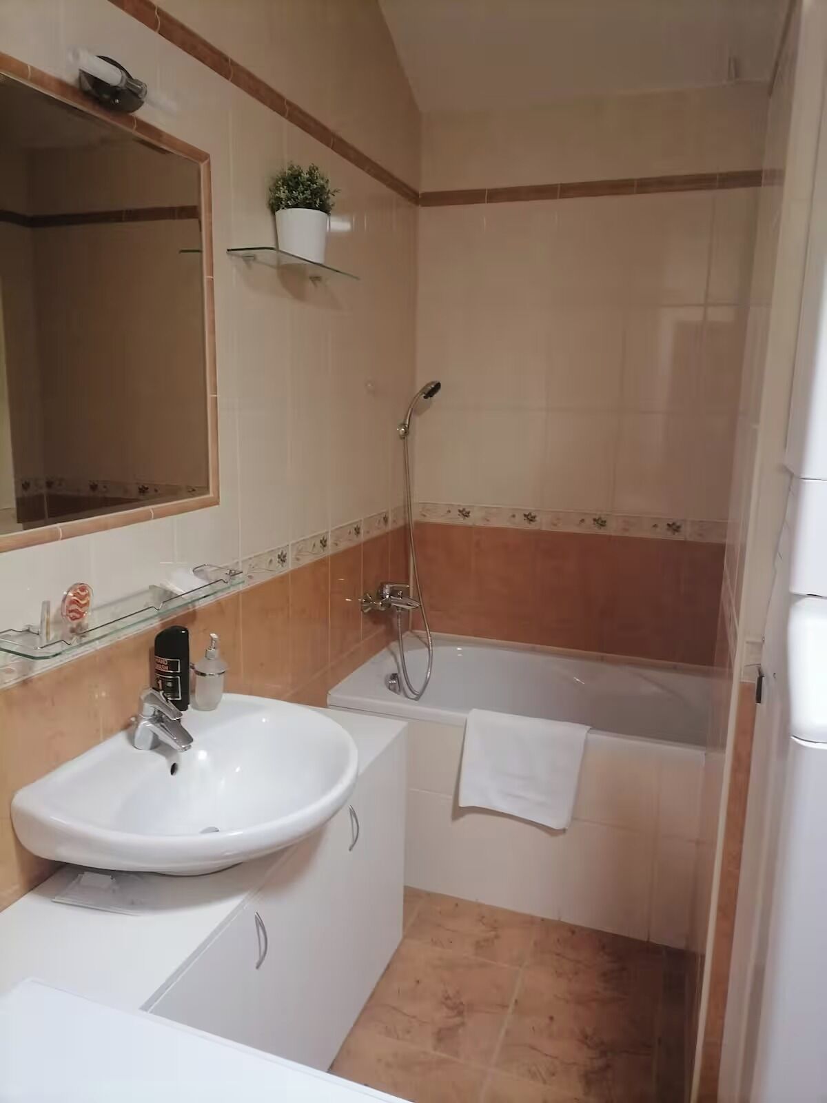 A bathroom with a sink, mirror, shower, and a towel hanging on the wall.