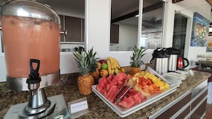 Mostrador de buffet con un tazón grande para ponche, diversas frutas y una estación de café.