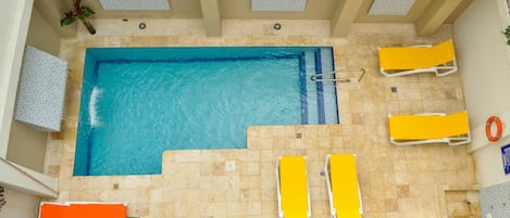An indoor swimming pool with a tiled floor, yellow lounge chairs, and a lifebuoy.