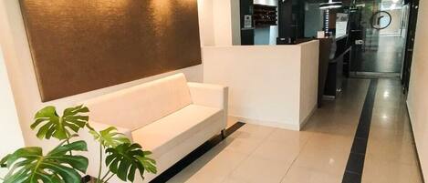 A modern hotel lobby with a white sofa, a large potted plant, and a reception desk.