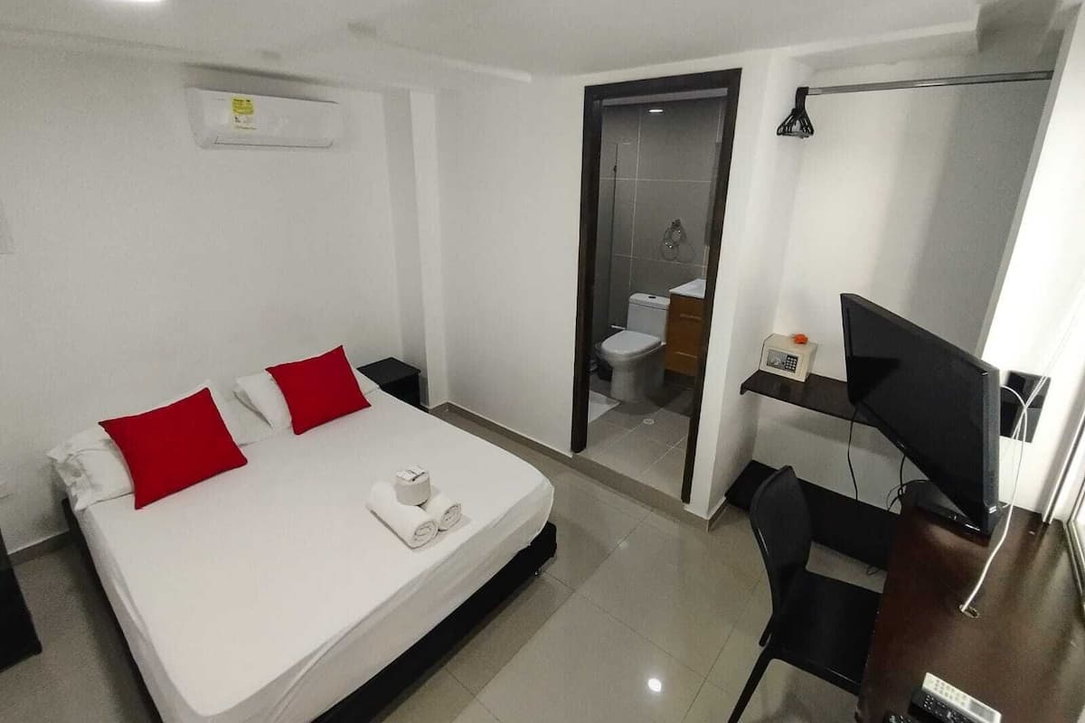 Une chambre d’hôtel avec un lit, un bureau et une chaise, une télévision et une salle de bain visible à travers une porte ouverte.