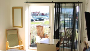 Een hotelkamer met een bed, een bureau en een stoel. Er is een balkon met uitzicht op boten en auto's.