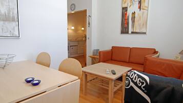 Ein modernes Wohnzimmer mit einer Couch, einem Esstisch mit zwei Schüsseln und einer Küche im Hintergrund.