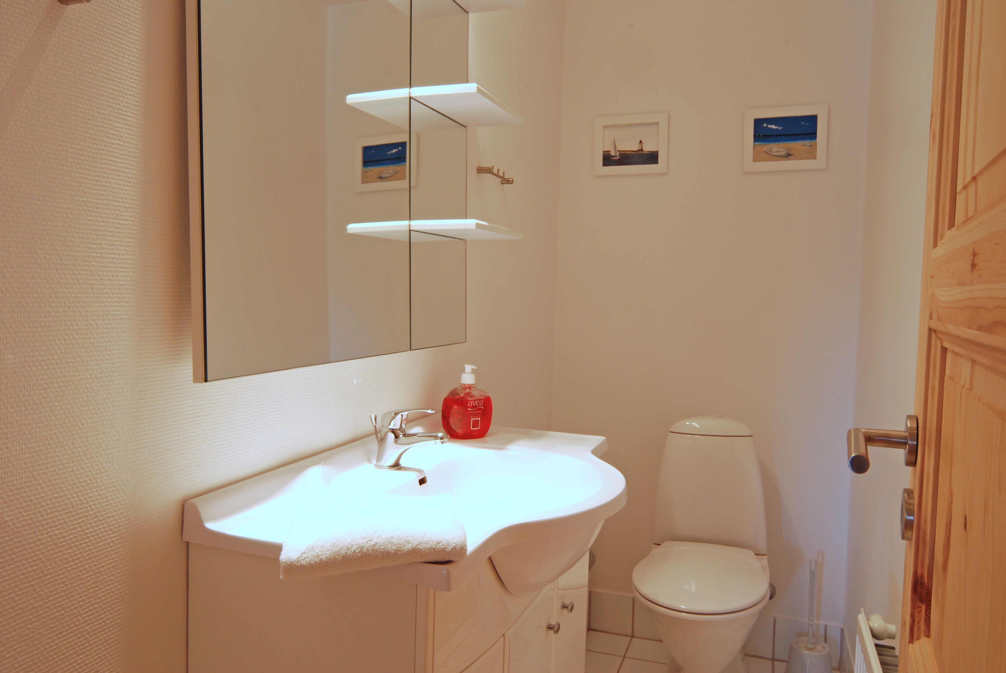 A bathroom with a white sink, mirror, and toilet. There are small framed pictures on the wall.