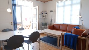 Een moderne woonkamer met een bank, een televisie, een eettafel met stoelen en een groot raam.