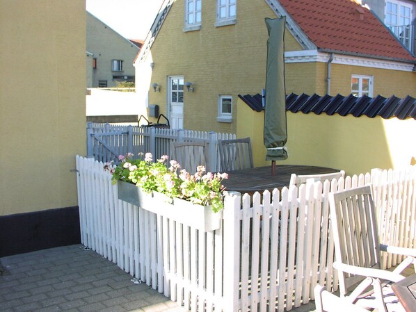 A patio area with a white picket fence, a table with chairs, and a planter box with flowers. - Skagen Apartment (Skagen)