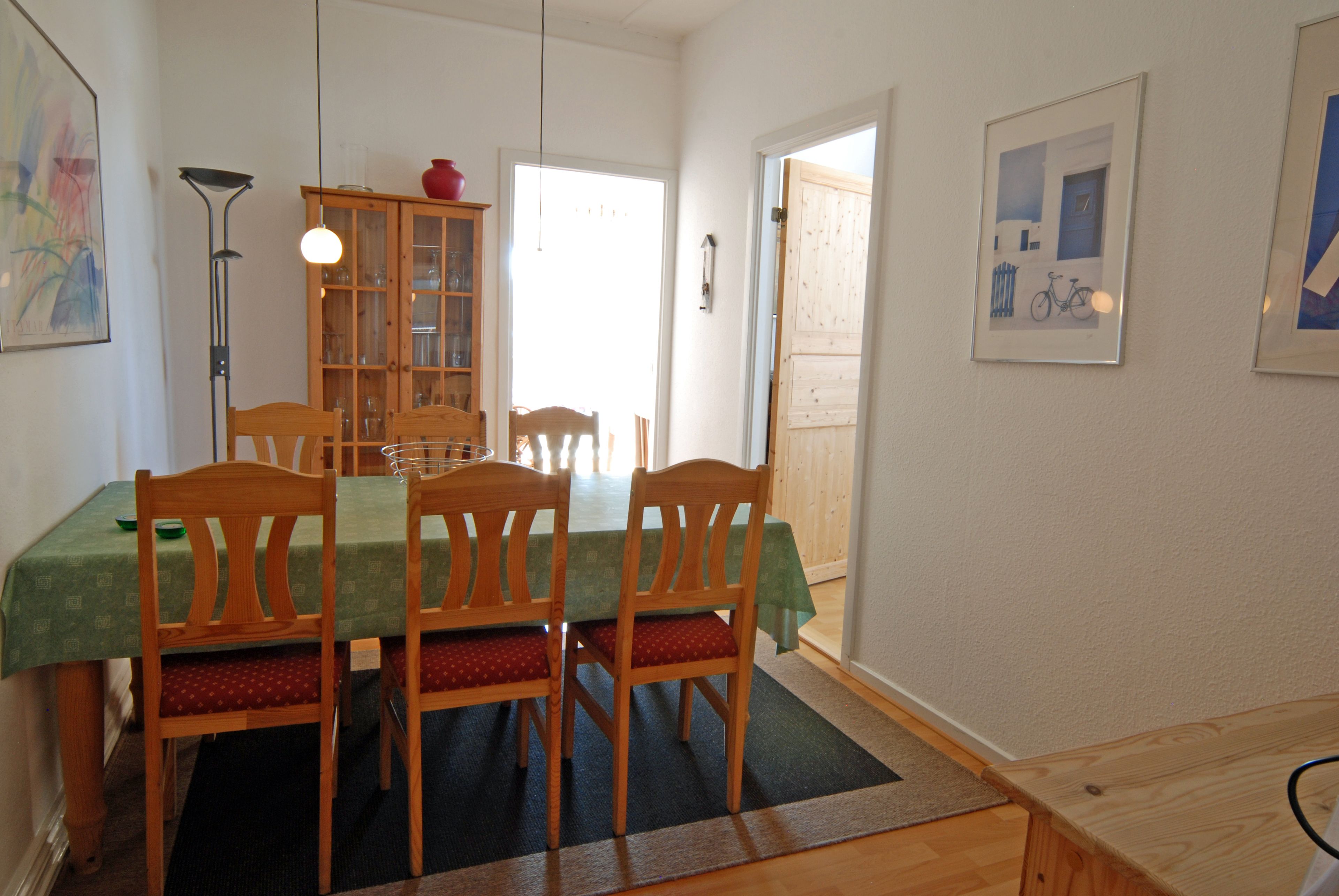 Un'area pranzo con un tavolo e sedie in legno, un mobile con ante in vetro e un quadro appeso al muro.
