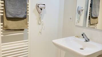 A modern bathroom with a white sink, a towel rack with a grey towel, a hairdryer, and a trash bin.