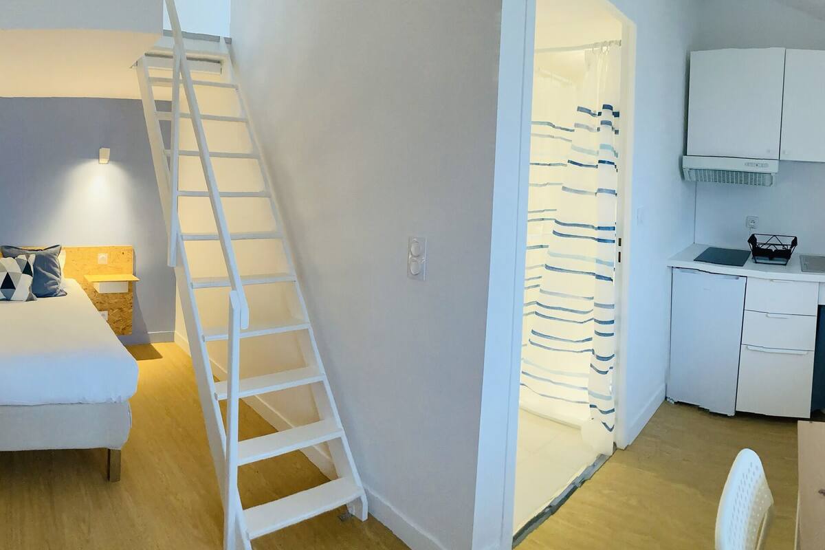Habitación de hotel compacta con cama, escritorio, televisor, escalera y kitchenette.