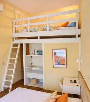 Ein Schlafraum mit Etagenbetten, einer Leiter, einem Schreibtisch, einem Stuhl und einem gerahmten Bild an der Wand.
