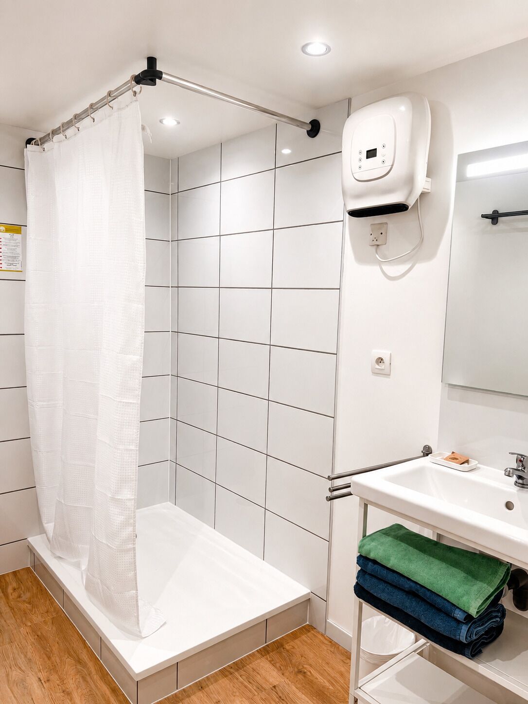 A modern bathroom with a shower, white tiles, a sink with a mirror, and a towel rack with folded towels.