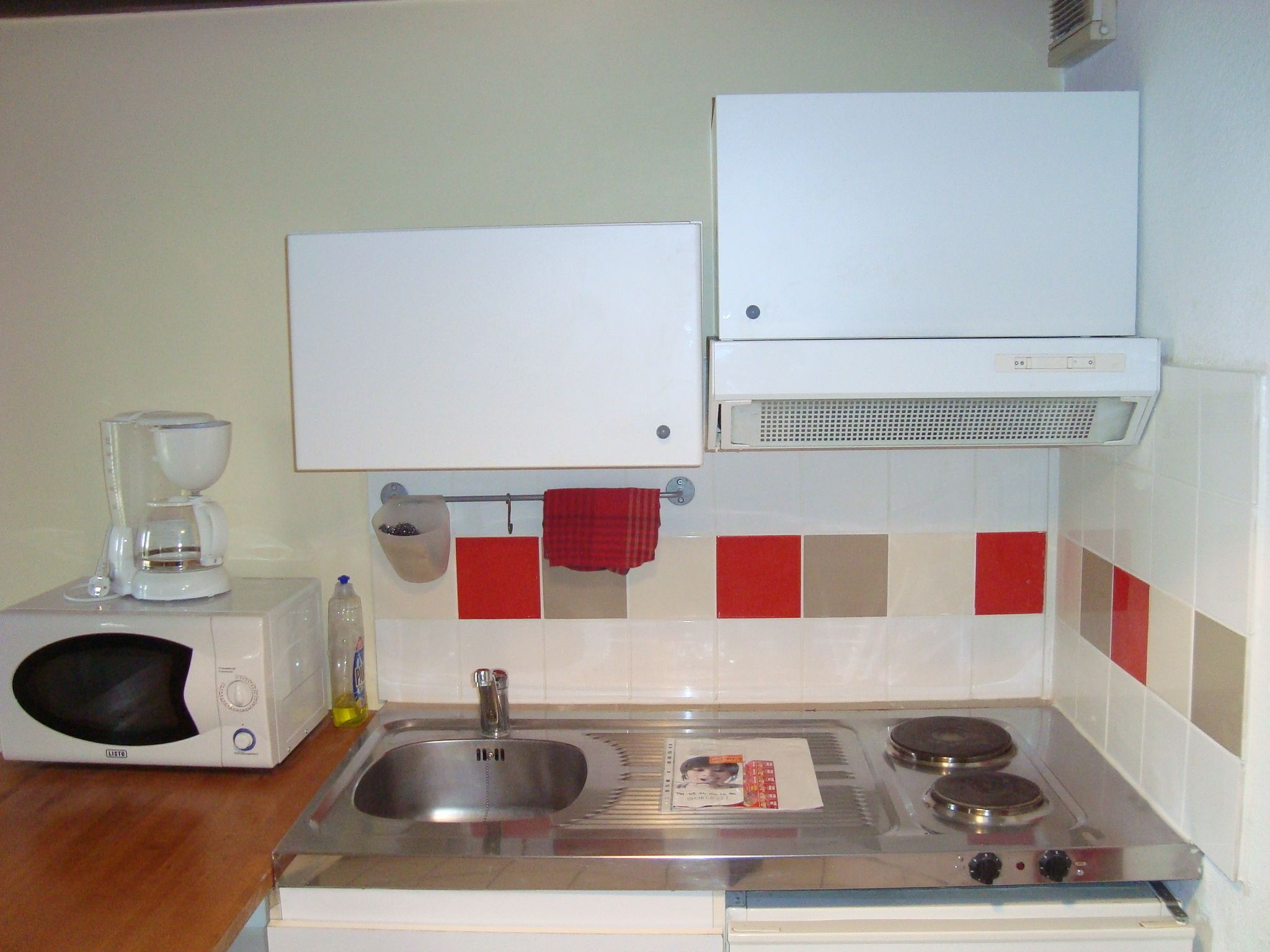 A kitchen with a microwave, sink, stove, and a whiteboard above the counter.