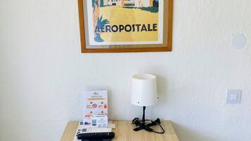 A framed poster of a Moroccan cityscape with an airplane, a lamp, and a remote control on a wooden table.