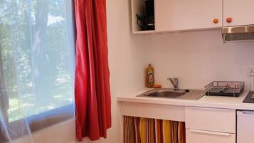 Una cocina compacta con un lavabo, una pequeña encimera y un ventanal con cortinas rojas.