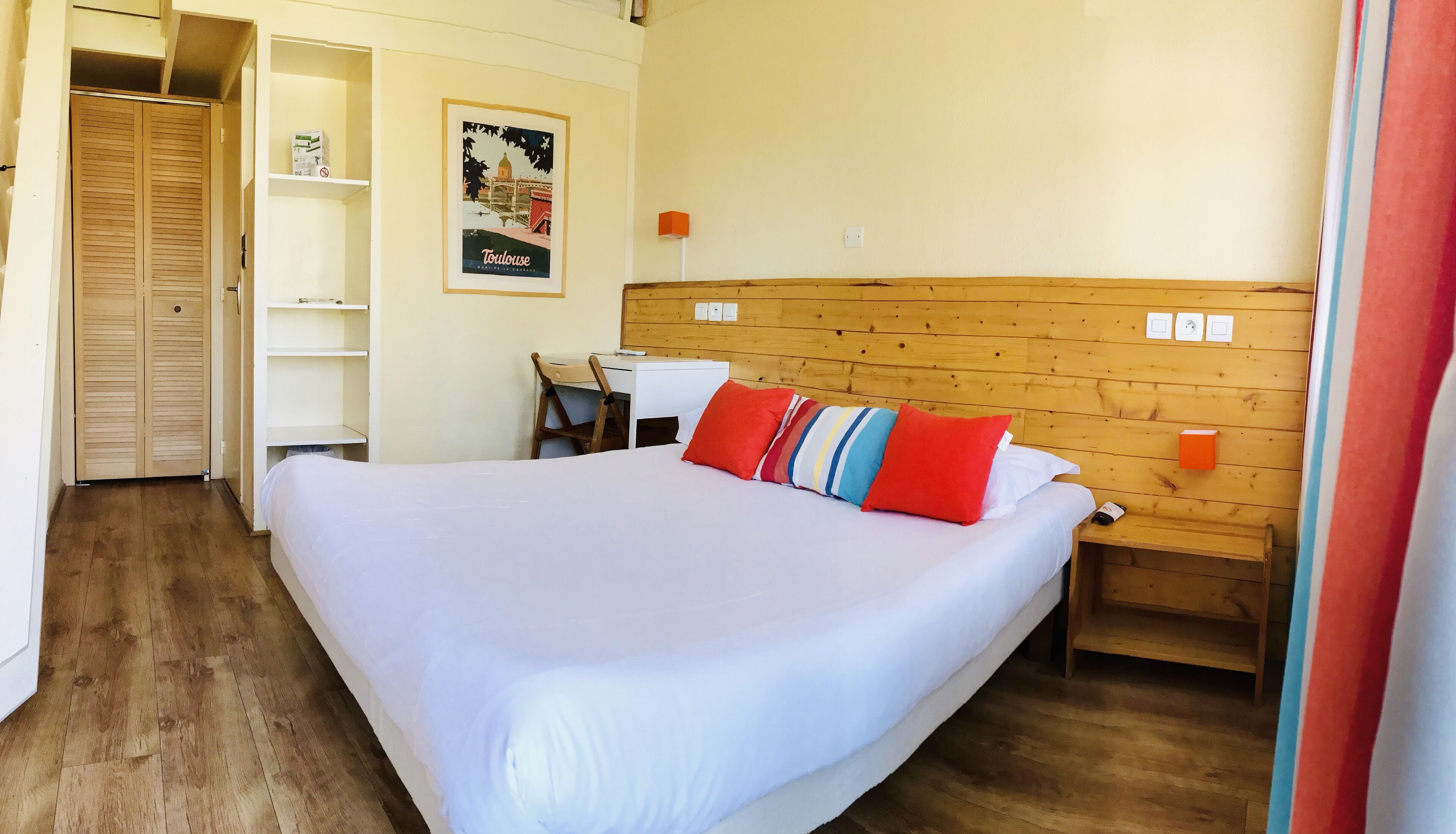 Habitación de hotel con una cama grande, cabecera de madera, escritorio con silla, armario y un cartel en la pared.