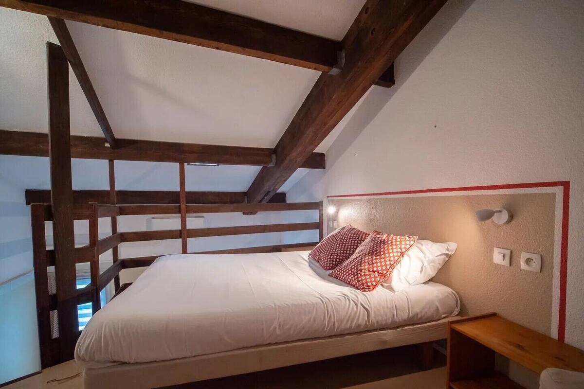 Un dormitorio con cama, almohadas, una mesita de noche, un banco de madera y vistas al cielo.
