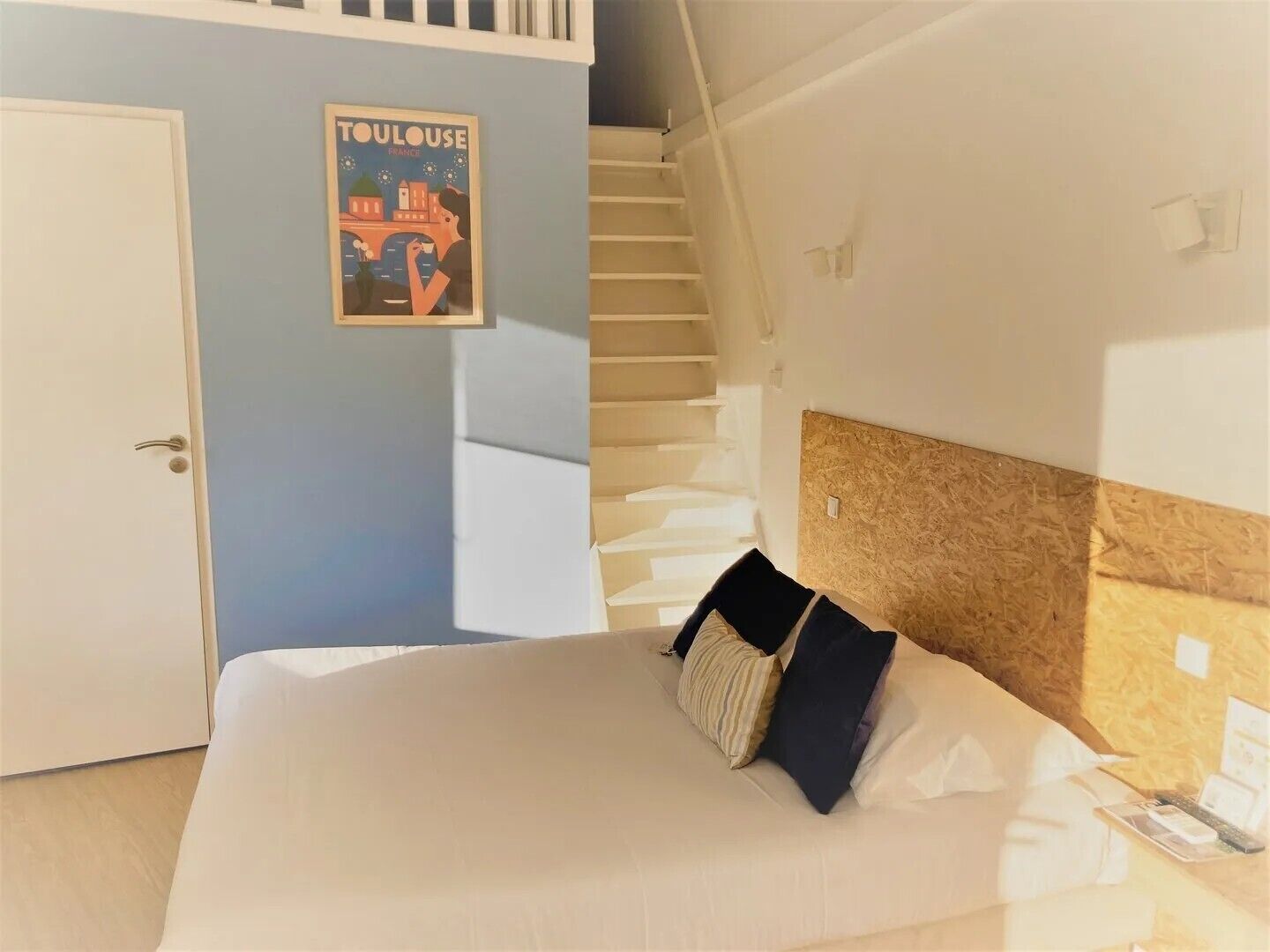 A bedroom with a bed, a poster on the wall, a staircase, and a door.