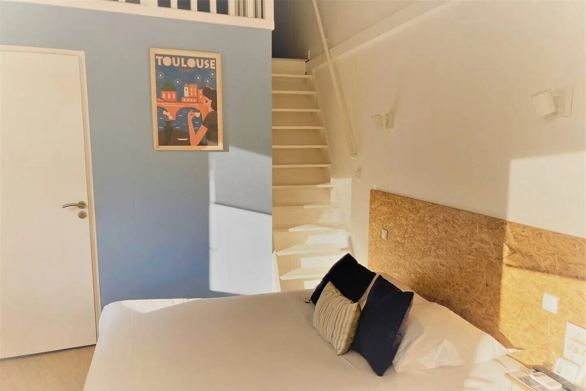Un dormitorio con una cama, un cartel en la pared, una escalera y una puerta.