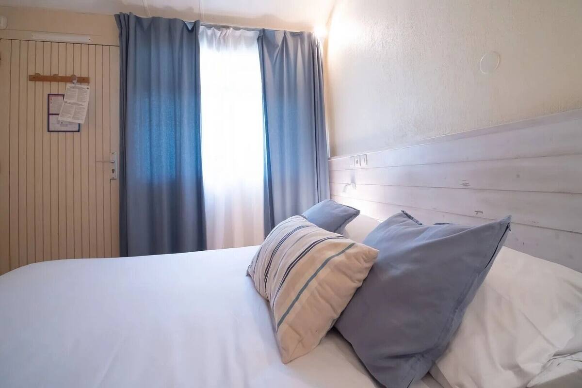 Una cama con almohadas, un cabecero de madera, una ventana con cortinas y un anuncio colgado en la pared.