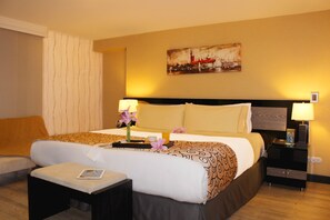 A hotel room with a large bed, two bedside tables, a nightstand, a small table with a lamp, and a painting on the wall.