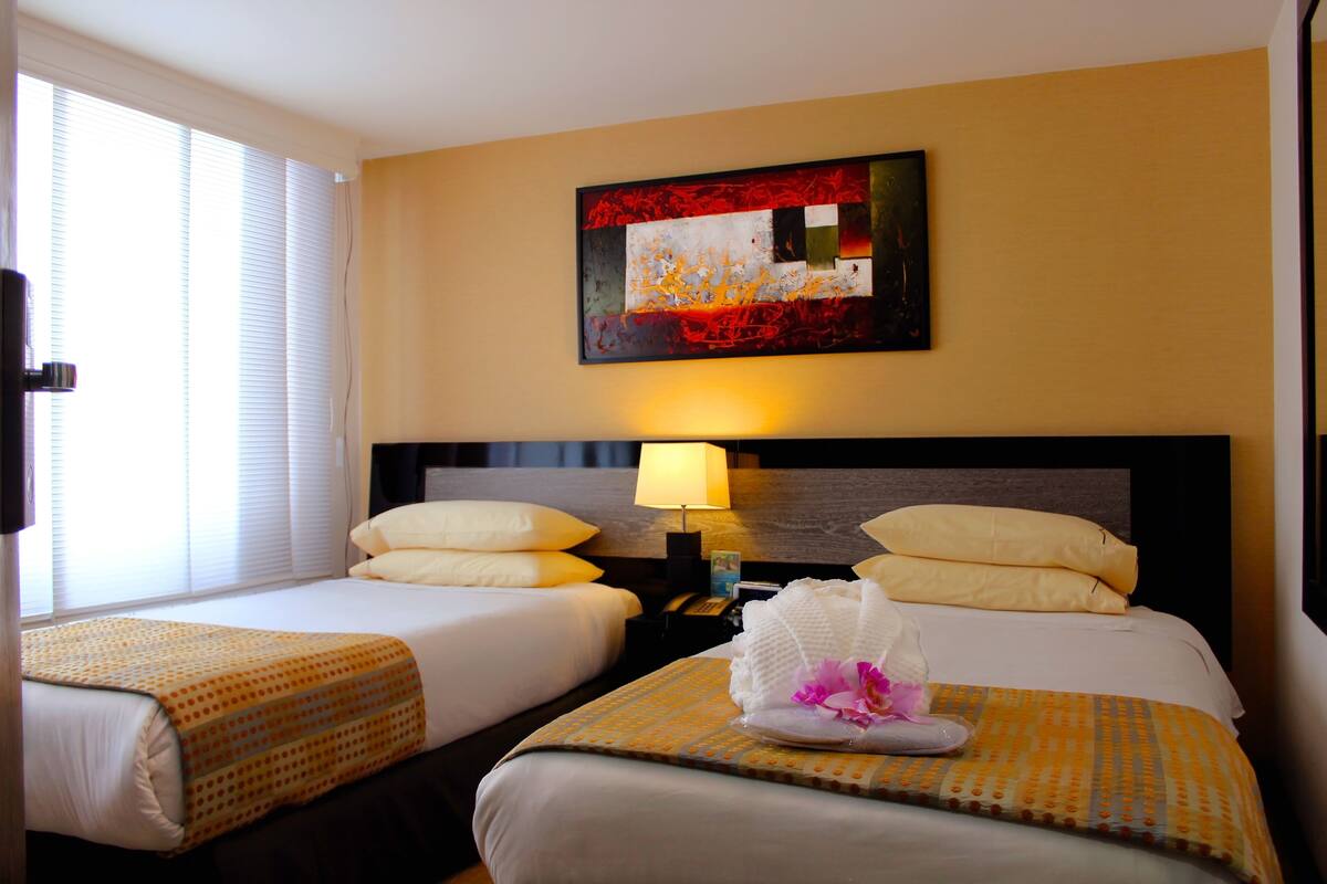 Une chambre d’hôtel avec deux lits, un tableau au mur, une lampe et un arrangement floral sur le lit.