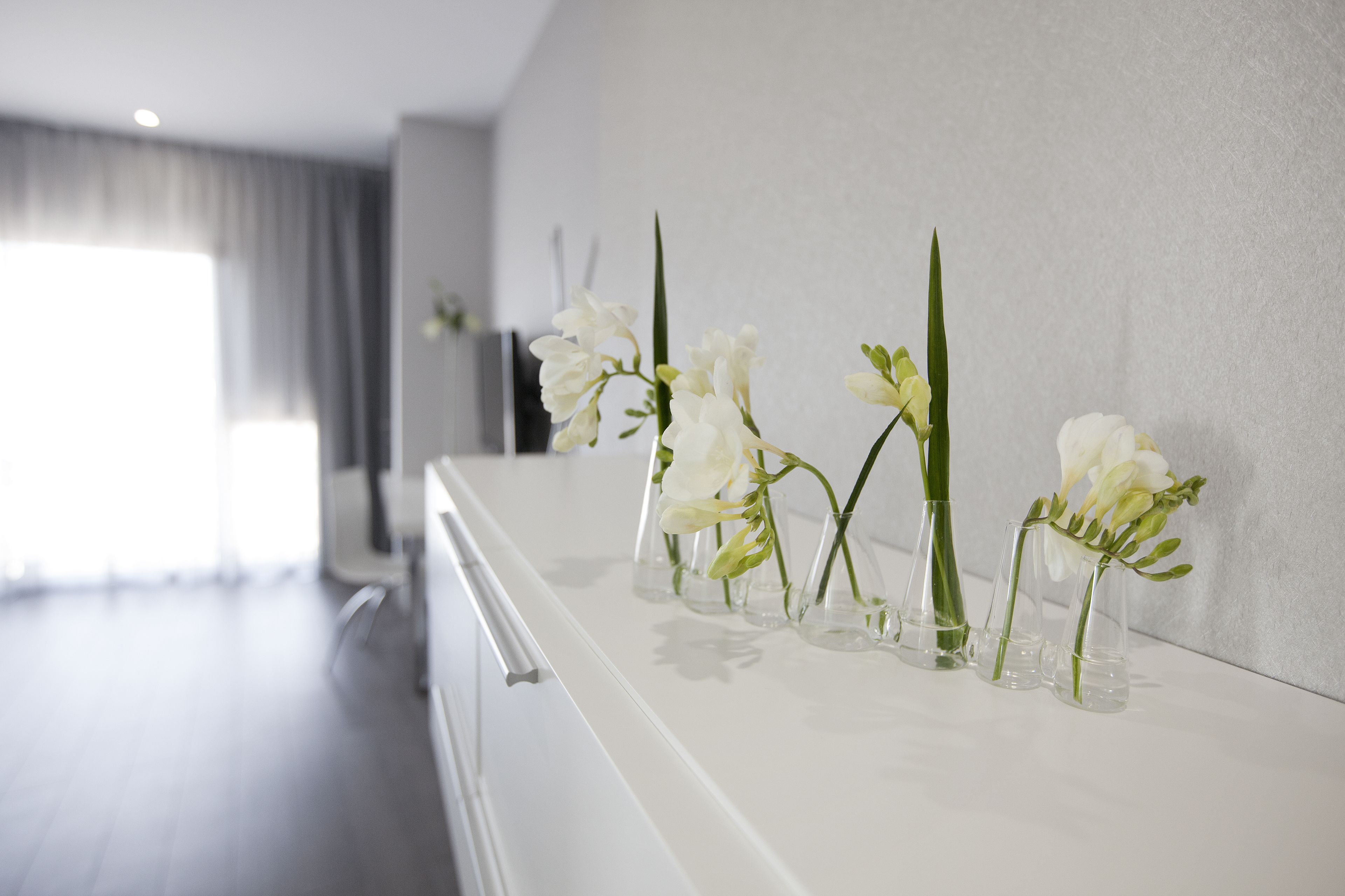 A modern bathroom with white fixtures and a row of clear glass vases with white flowers on a white countertop.