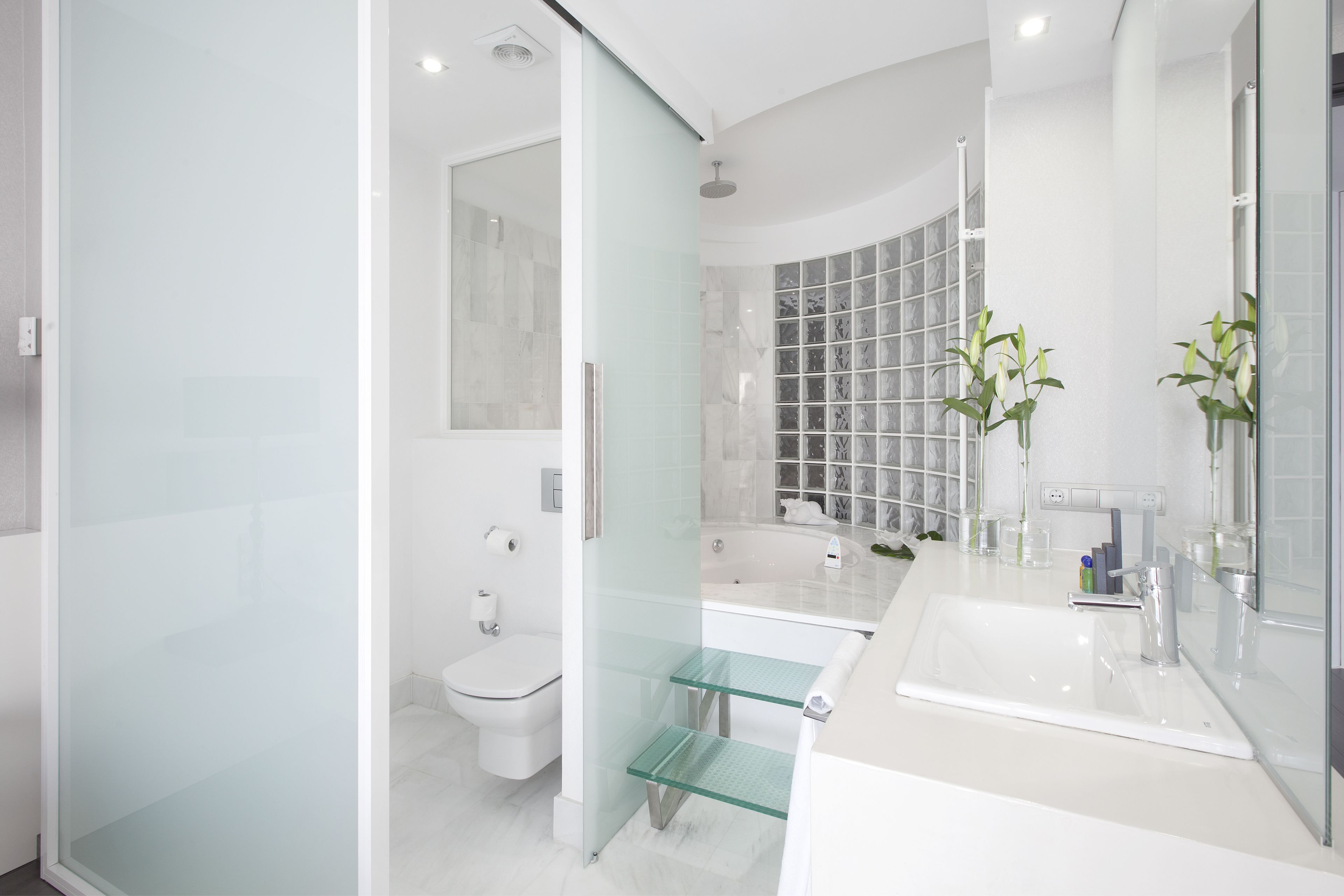 Un baño moderno con cabina de ducha de vidrio, un lavamanos blanco con un espejo grande y un inodoro.