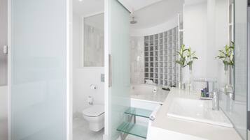 Un baño moderno con cabina de ducha de vidrio, un lavamanos blanco con un espejo grande y un inodoro.