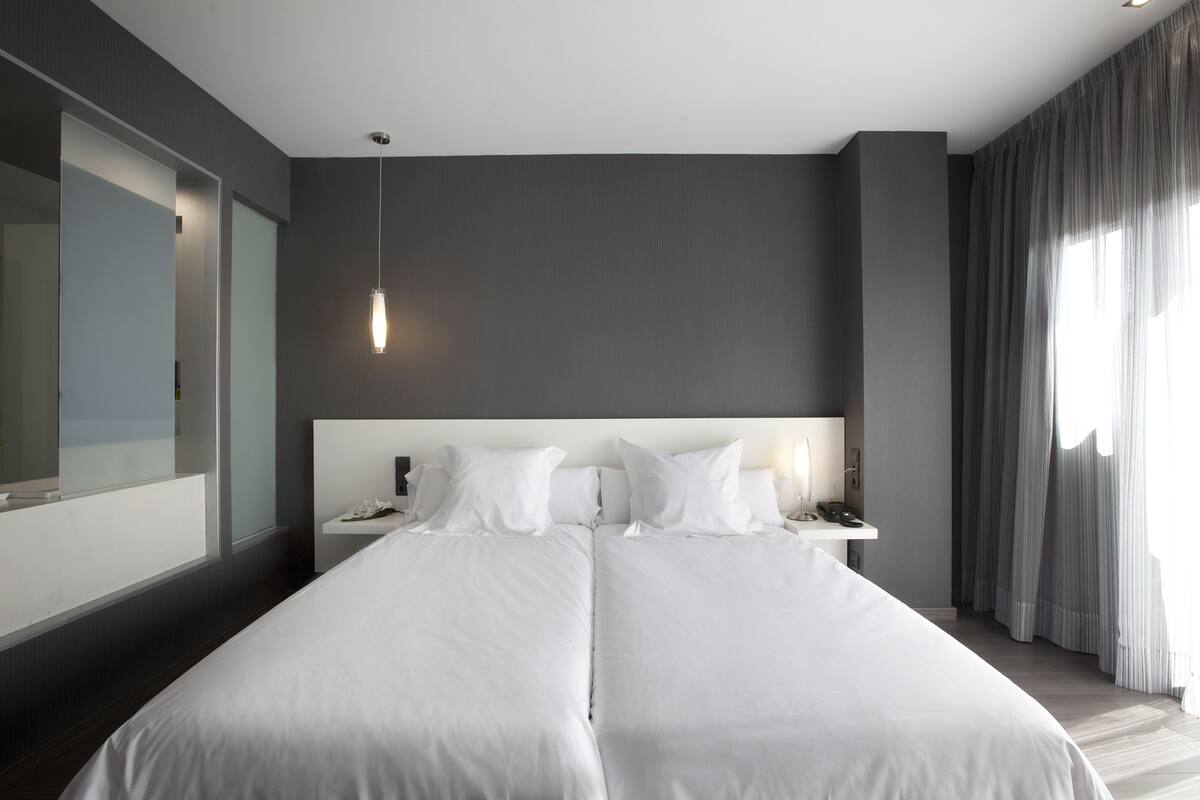 A modern hotel room with a large bed, bedside tables, a mirror, and a hanging light fixture.