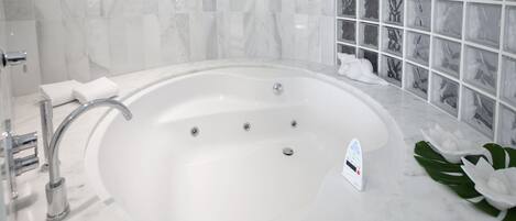 Une salle de bain moderne avec une grande baignoire blanche, une douche en verre et un mur recouvert de carreaux de marbre.