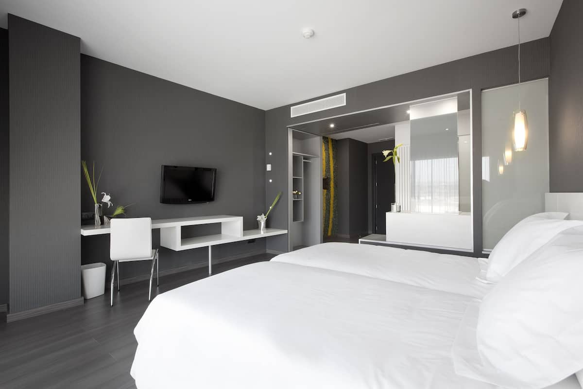 A modern hotel room with a large bed, a flat-screen TV, a desk, and a mirror.